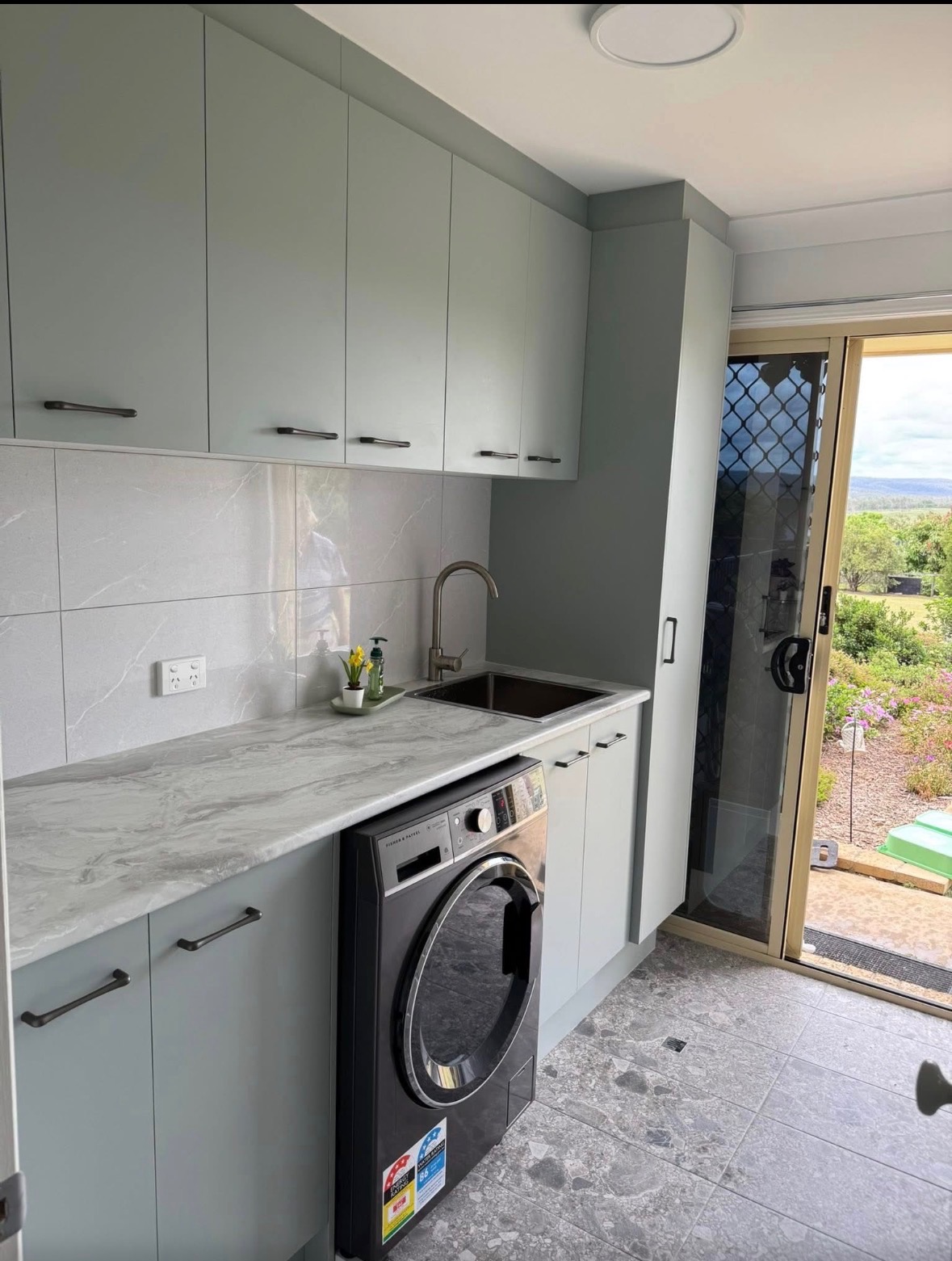 Sage-green custom laundry cabinetry with stone bench — PMG Cabinetry