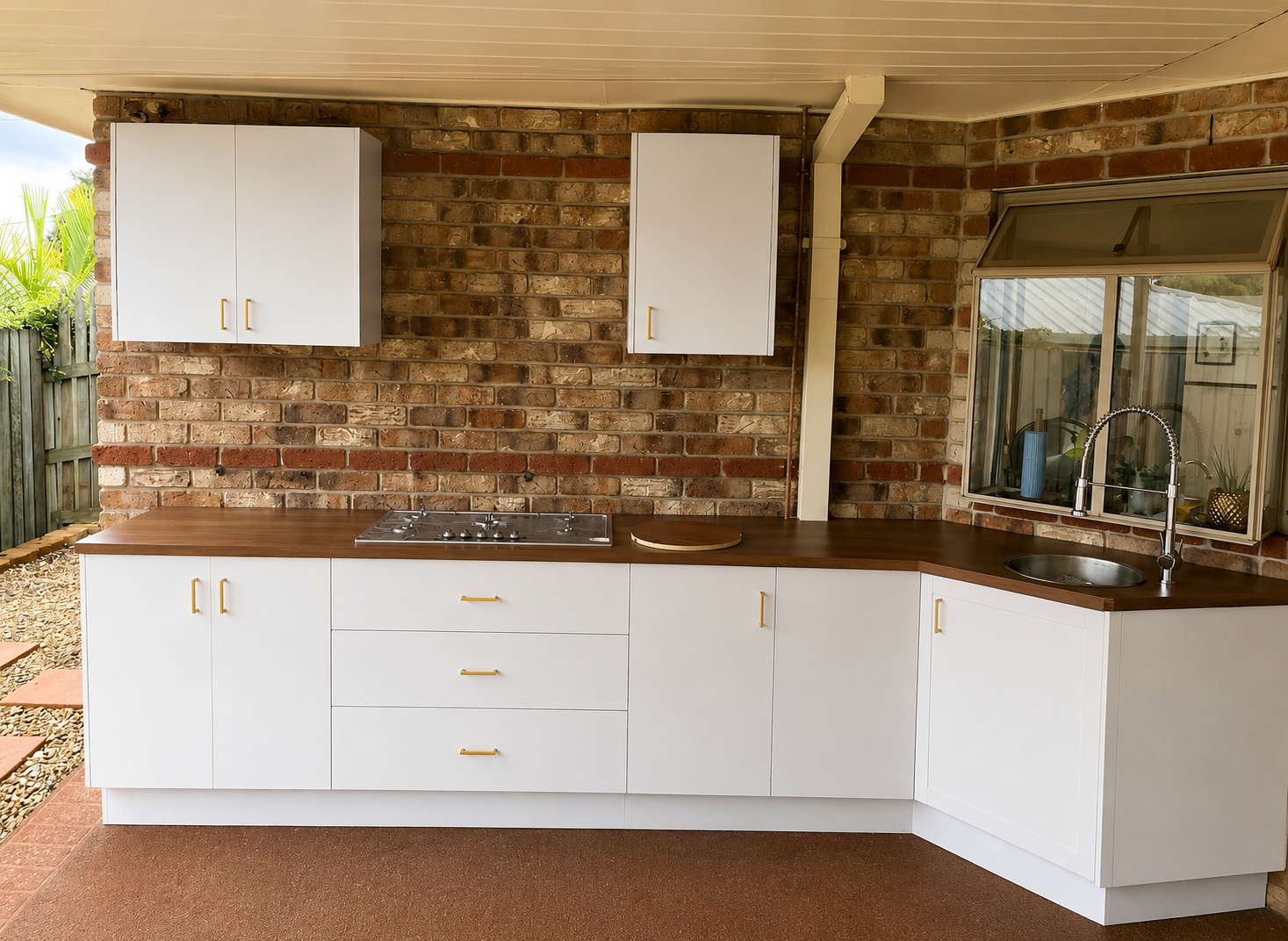 Outdoor alfresco kitchen with white Shaker cabinetry, timber benchtop, gas cooktop and undermount sink against exposed brick — PMG Cabinetry