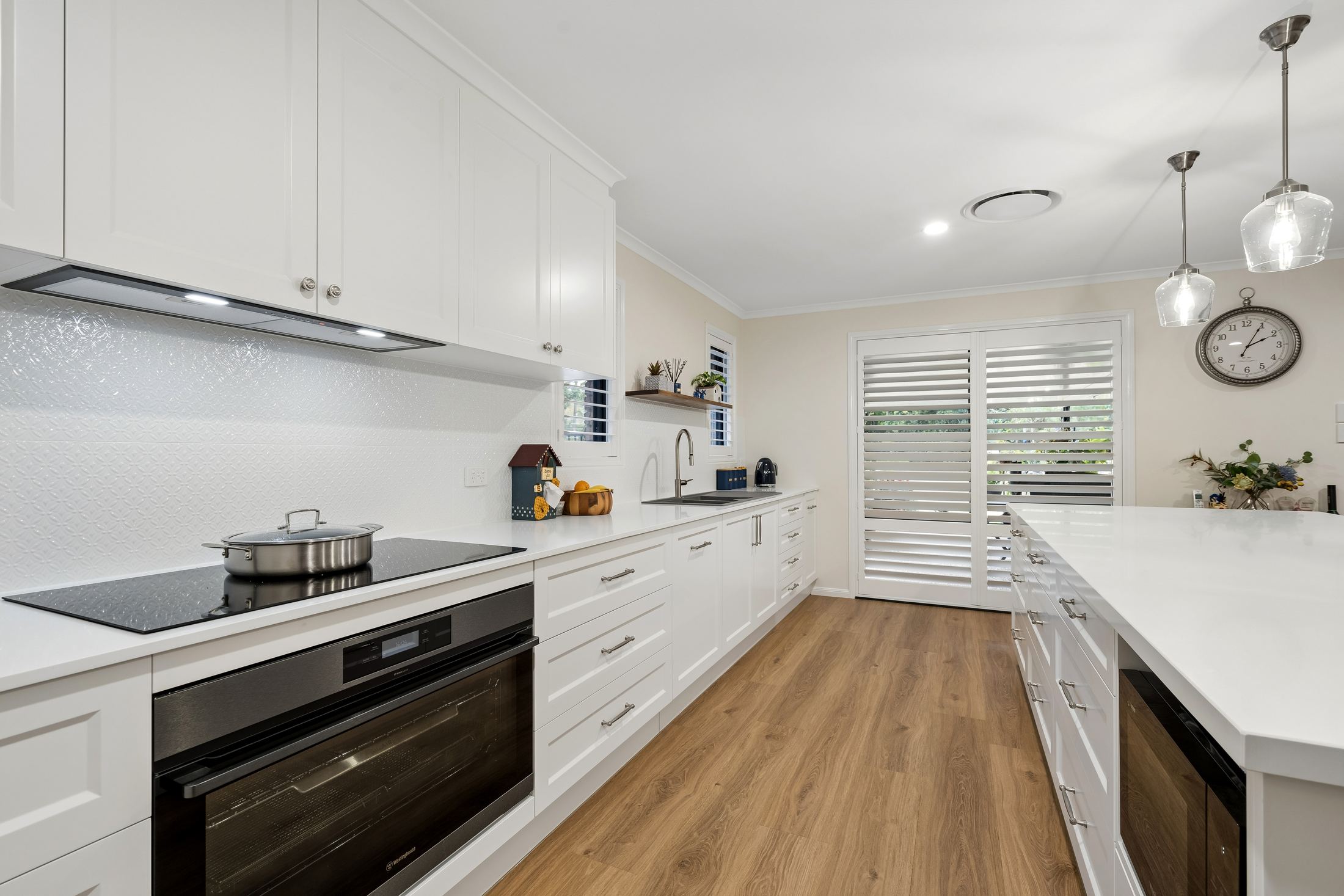 Induction cooktop and wall oven in white Shaker cabinetry — PMG Cabinetry
